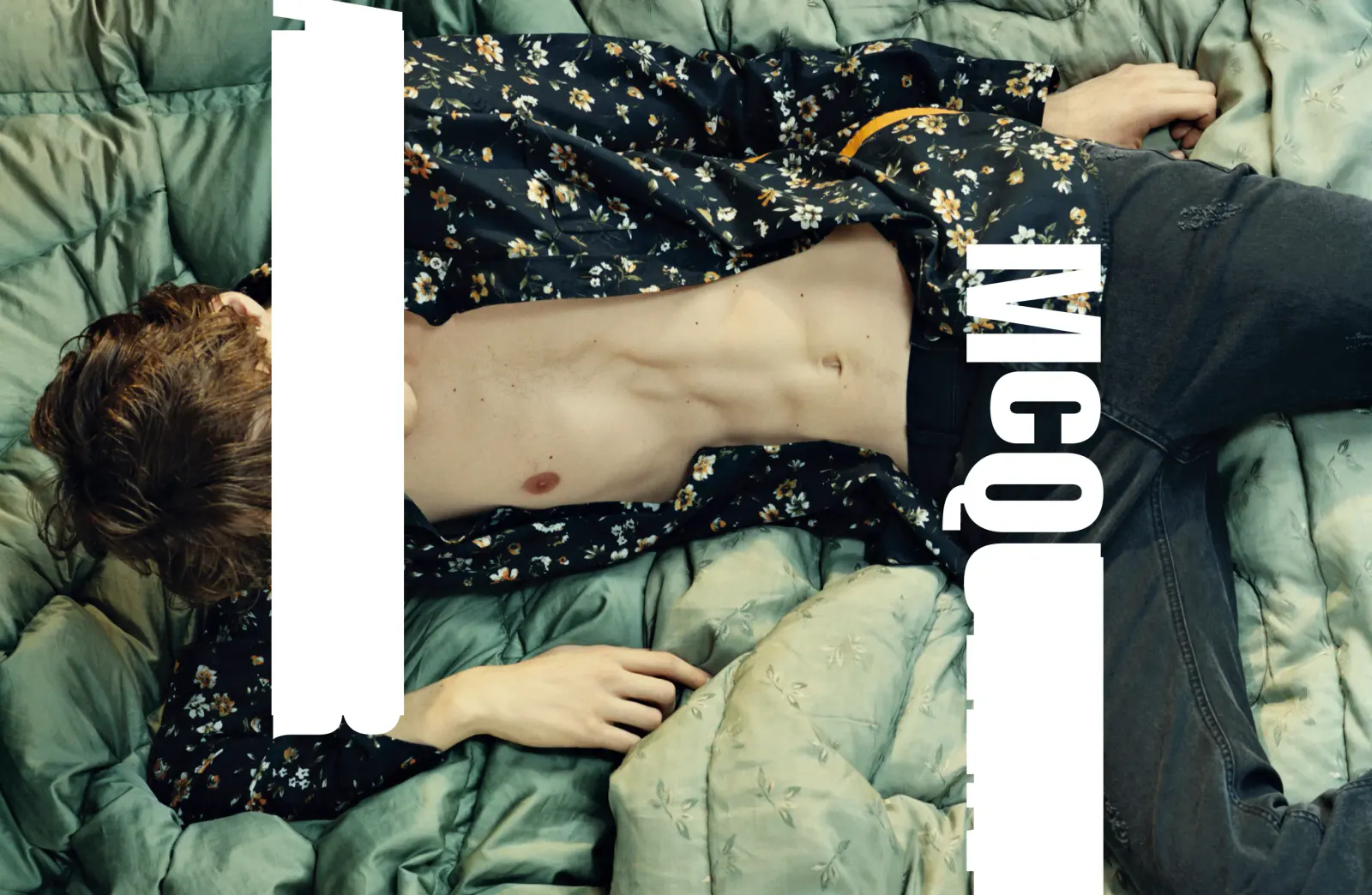 McQ campaign photograph: a model lying on a green quilted blanket in a floral shirt, overlaid with a large white McQ wordmark and a white bar