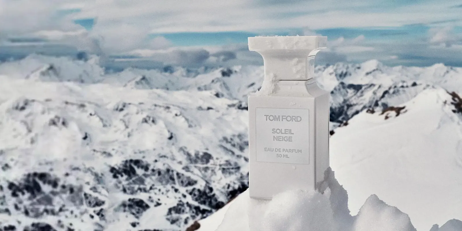 Tom Ford Soleil Neige campaign photograph: a white fragrance bottle standing in snow in front of snowy mountains